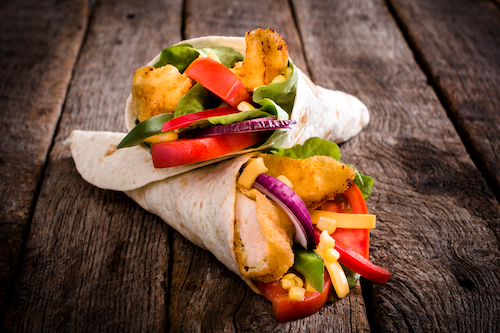 Tortilla wrap sandwich with fried chicken and vegetables on wooden background,selective focus