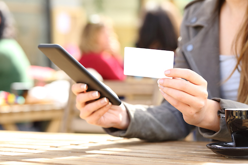 Close up of woman hands holding smart phone and blank credit card in a bar